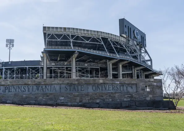 Exterior view of Penn State stadium with stone sign reading 'PENNSYLVANIA STATE UNIVERSITY' in front and metal seating in the background